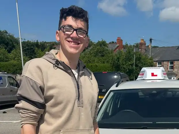 Young man in Rhyl next to driving instructor's car after completing driving lessons