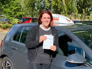 Young woman standing by instructor's car in Mold proud with driving test pass certificate