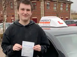 Young man standing by instructor's car with pass certificate at driving test centre in Chester