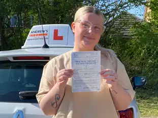 A young woman smiling proudly beside her driving instructor’s car in Wrexham, holding up her new driving test certificate, celebrating the end of her driving lessons in Wrexham.