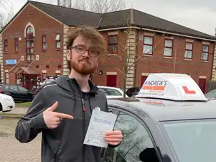 Man pointing at his driving test pass certificate outside the test centre