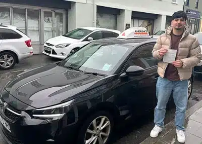Mansoor from Holyhead standing next to instructor Geraint Jones's car holding his first-time driving test pass certificate.
