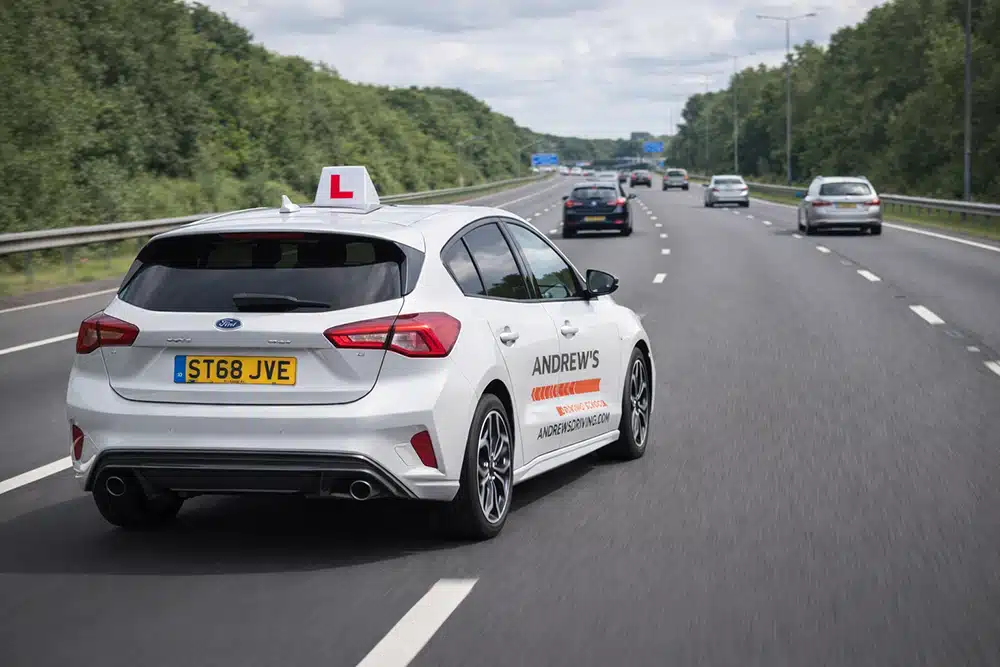 Driving school car on busy motorway Andrew’s Driving School learner car driving on a busy motorway with L-plate on the roof