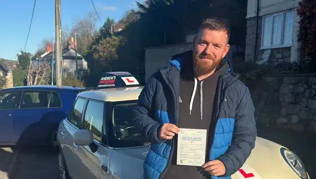 Jonny holding his driving test pass certificate in Rhyl, standing beside an Andrew’s learner car