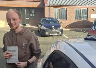 Noah smiling with his driving test pass certificate in Rhyl after passing with Andrew's Driving School instructor Paul Sanders.