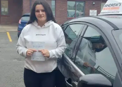 Maya Leece holding her driving test pass certificate beside Peter’s driving school car at Rhyl Driving Test Centre.