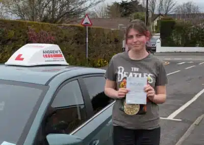 Jessica holding her practical driving test pass certificate beside a learner car in Colwyn Bay after passing her test in Rhyl.