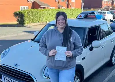 Roxanne holding her driving test pass certificate at Rhyl Driving Test Centre with Jimmy’s automatic car