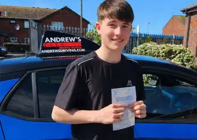Zac Hewitt holding driving test pass certificate at Rhyl Driving Test Centre next to blue driving school car