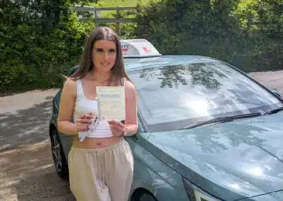 Ayme holding a driving test pass certificate beside a car after passing first time in Rhyl with Jack.
