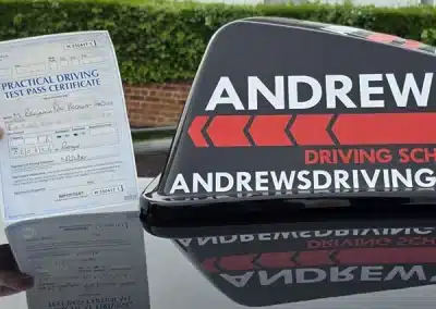 Driving test pass certificate displayed next to Andrew’s Driving School learner car sign in Conwy