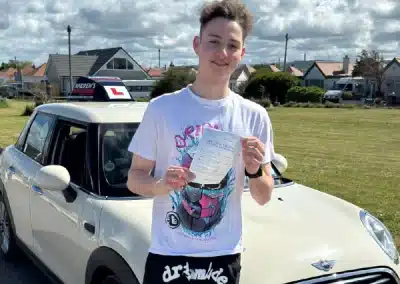Freddie from Kinmel Bay holding his automatic driving test pass certificate after passing in Rhyl with instructor Jimmy.