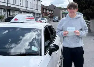 Harri from Old Colwyn holding his driving test pass certificate beside Marcus’s car after passing his test