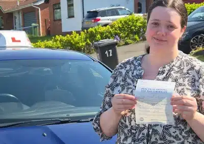 Jasmine holding her driving test pass certificate beside a learner car after passing first time in Wrexham.