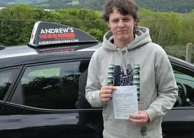 Jayden standing beside an Andrew’s Driving School car holding a practical driving test pass certificate after passing first time with 0 minors alongside instructor Jamie Abba