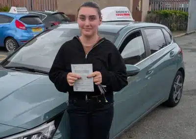 Meg Wylde holding her driving test pass certificate beside a car after passing in Rhyl with Jack.