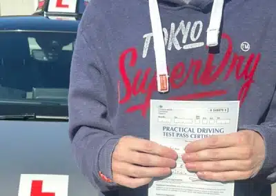 Sean holding practical driving test pass certificate at Rhyl Driving Test Centre with learner car