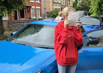 Chloe proudly holds her driving test pass certificate after achieving a first-time pass at Rhyl Driving Test Centre with instructor Ryan.