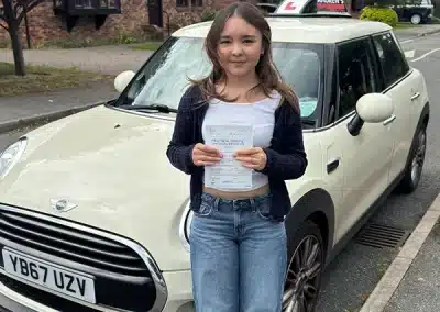 Sophie holding her driving test pass certificate beside Fiona’s automatic learner car after passing her driving test in Rhyl