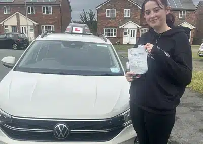 Francheska holding her driving test pass certificate beside Paul Singleton’s learner car after passing her driving test in Rhyl.