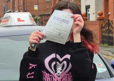 Isabel holding her driving test pass certificate beside Craig’s Andrew’s Driving School car after passing her driving test in Wrexham.