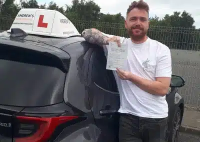Kieran holding his driving test pass certificate beside Barry’s Andrew’s Driving School car after passing his driving test in Bangor with zero driving faults.