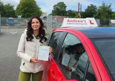 Layla holding her driving test pass certificate beside Claire’s Andrew’s Driving School car after passing first time in Bangor.