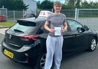 Richard holding his driving test pass certificate beside Geraint’s learner car after passing his driving test in Bangor with zero driving faults.