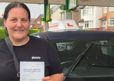 Siobhan proudly holds her driving test pass certificate beside Craig’s learner car after passing first time in Wrexham.
