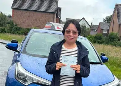 Sophie holding her driving test pass certificate beside Fiona’s automatic learner car after passing her driving test in Rhyl.