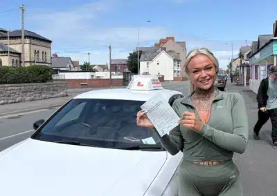 Zena proudly holds her driving test pass certificate beside Marcus’s learner car after passing first time at Rhyl Driving Test Centre.