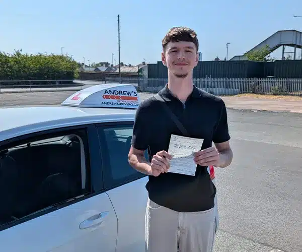 Artem in Rhyl smiling and holding his driving test pass certificate next to Tomas Kapus's white driving tuition Golf