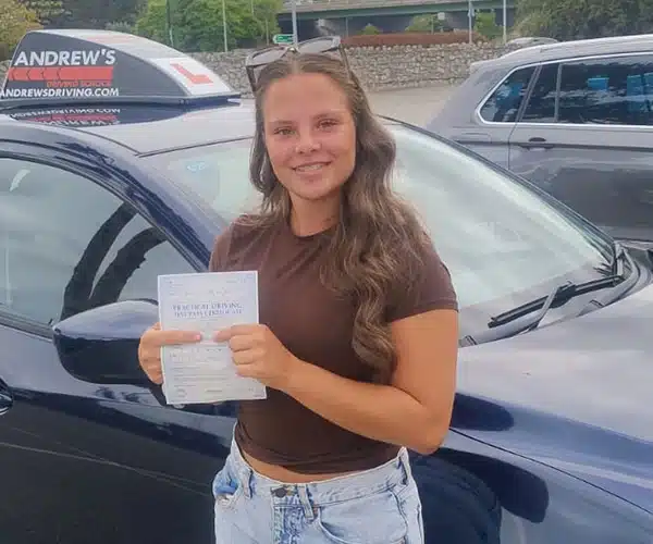 Beth celebrating her driving test pass in Rhyl beside her instructor Mark Bilton’s Andrew’s Driving School car.