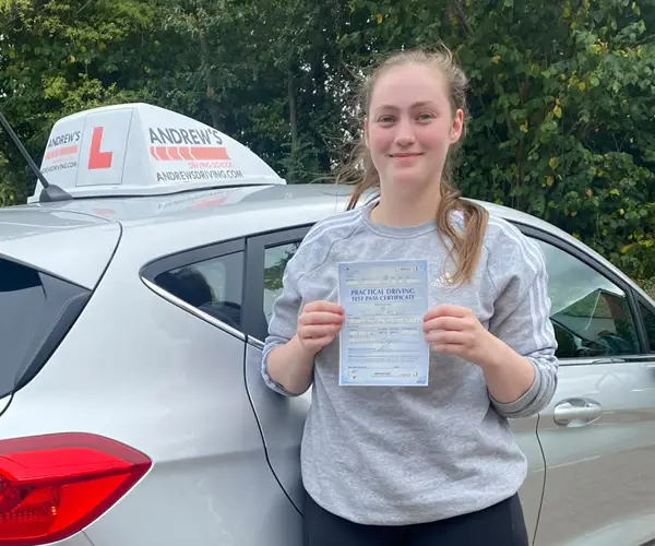 Lucyanna Mcabe holding her practical driving test pass certificate beside an Andrew’s Driving School car after passing her driving test in Wrexham with instructor Karl Whitefoot.