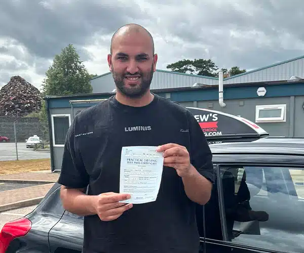 Luke Watson showing off his driving test pass certificate by Llinos's car in Bangor Driving Test Centre