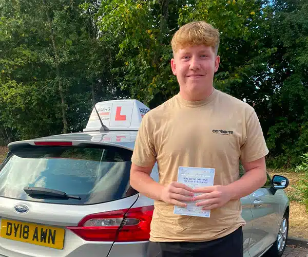 Learner driver Luke celebrating a first-time driving test pass in Wrexham with instructor Karl beside an Andrew’s Driving School car.