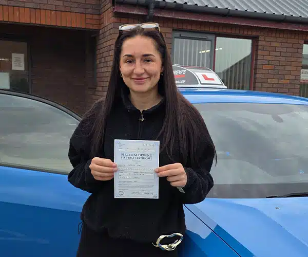 Jessica outside Rhyl Driving Test Centre with Ryan's blue Audi, holding her new driving test pass certifate