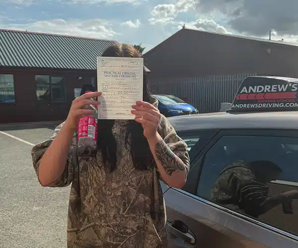 Jessica outside Rhyl Driving Test Centre holding her pass certificate in front of her face standing next to Ursula's Toyota.