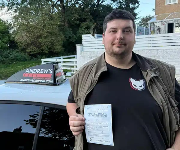 Brandon holding his driving test pass certificate, standing next to Ben's white BMW in Rhyl