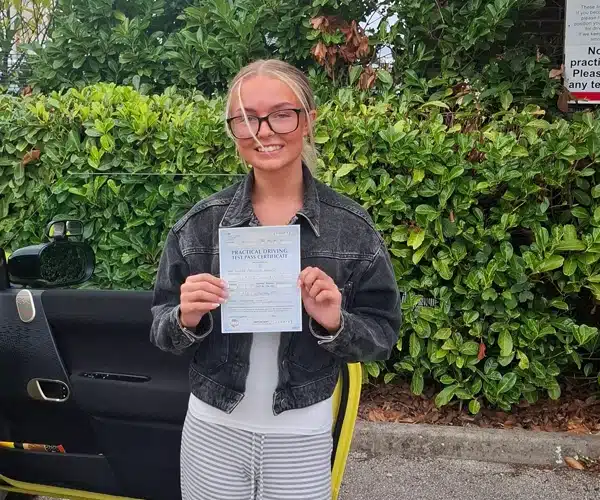 Kaydee in Barnsley Driving Test Centre, smiling with her pass certificate stood next to Janets automatic tuition car 