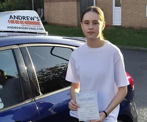 Maisie Jones holding her driving test pass certificate beside an Andrew’s Driving School car after passing in Wrexham