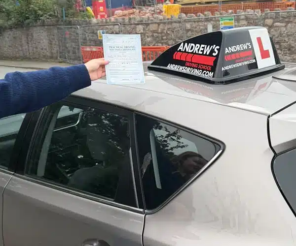 Mia Jones from Abergele holding her pass certificate beside an Andrew’s Driving School tuition car after passing at Rhyl Test Centre