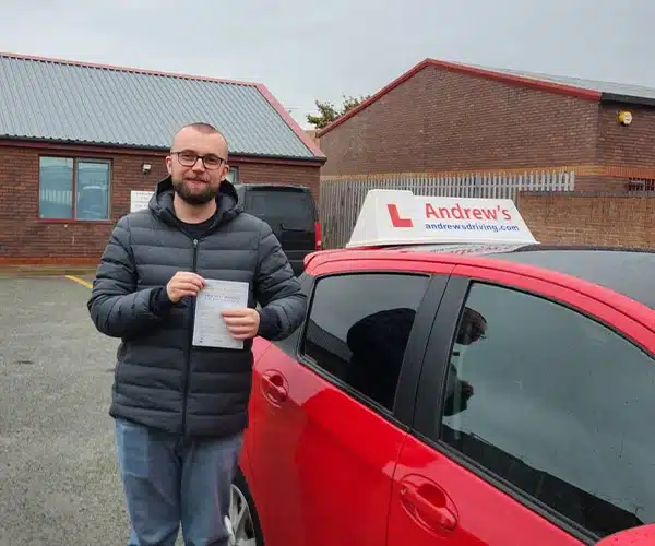 Stephen Robertson outside Rhyl Driving Test Centre holding his pass certificate beside Claire’s red Toyota Yaris
