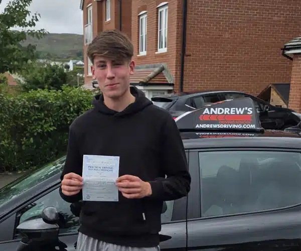 Alfie from Conwy holding his pass certificate beside Jamie’s Andrew’s Driving School car after passing at Bangor Test Centre