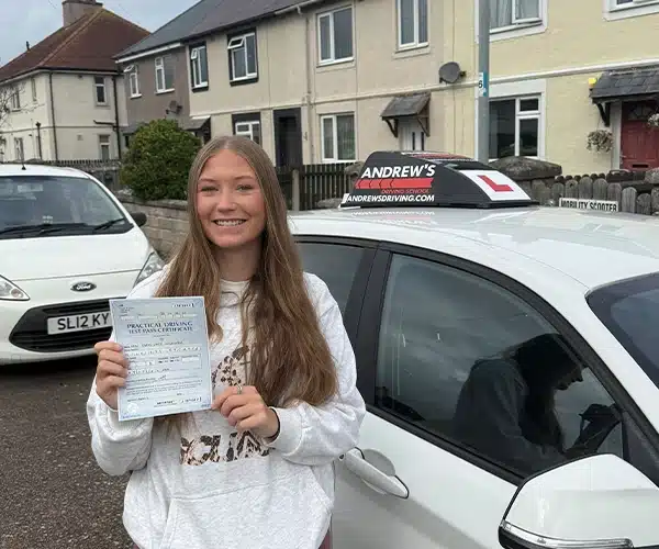 Carys Wilkinson standing holding her driving test pass certificate by Bens driving tuition car in Llandudno 