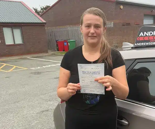 Charlie Clifton from Kinmel Bay in Rhyl Driving Test Centre holding her pass certificate by Ursula's Andrew's Driving School car
