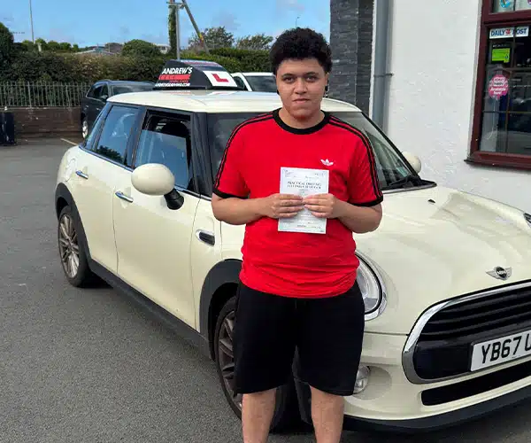 Ezrah Williams holding his driving test pass certificate in Rhyl beside instructor Jimmy Garland’s automatic Mini.