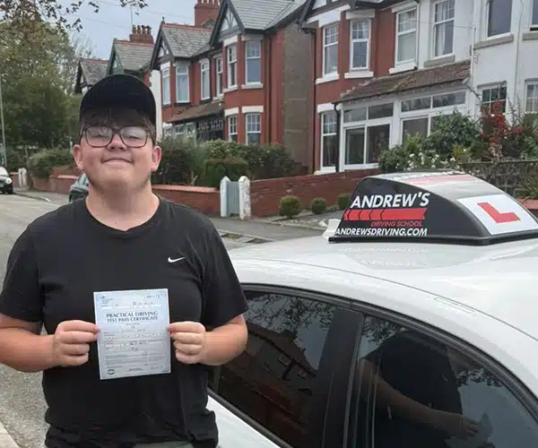 Liam Ware holding his pass certificate beside Ben’s Andrew’s Driving School car in Colwyn Bay after passing his test in Rhyl