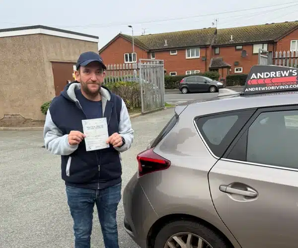 Marc Cunliffe from Abergele in Rhyl Driving Test Centre holding his pass certificate by Ursula's Andrew's Driving School car