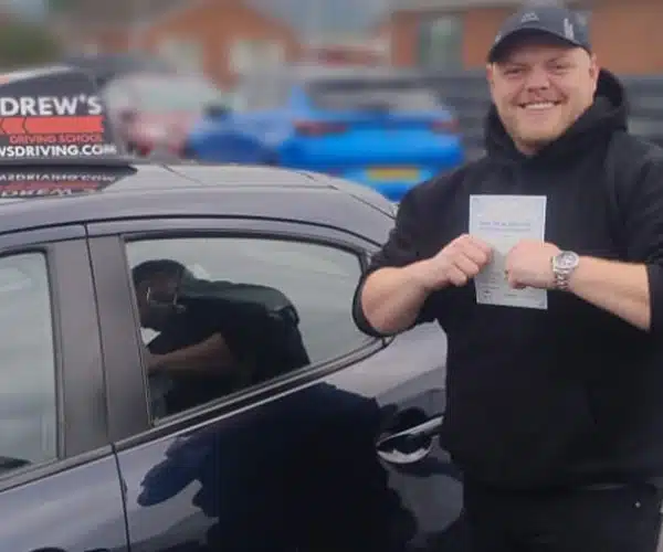 Matthew smiling with his driving test pass certificate by Mark Biltons tuition car at Rhyl Driving Test Centre